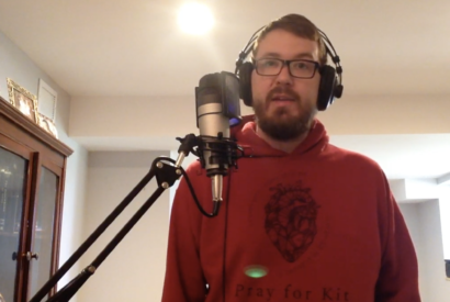 Bryan stands in front of a microphone recording the episode.